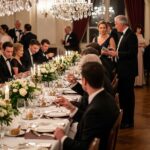 formálne banketové stolovanie s hosťami v spoločenskom oblečení pri dlhej tabuli a krištáľovom lustri