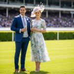 Muž v obleku a žena v šatách stoja s pohármi šampanského na dostihovej dráhe.