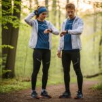 Muž a žena v bežeckom oblečení na lesnej ceste za ranného svetla, žena si upravuje čelenku.